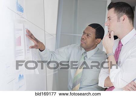 Stock Photo - Businessmen examining charts on office wall. Fotosearch