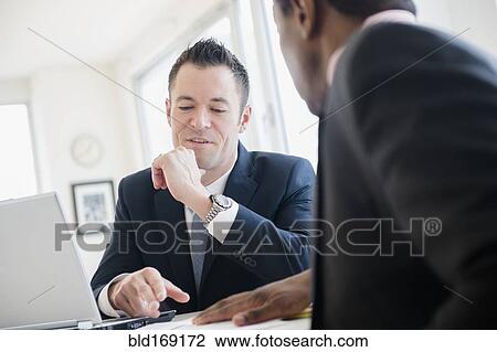 Businessmen talking at desk in office View Large Photo Image Stock Image - Businessmen talking at desk in office. Fotosearch