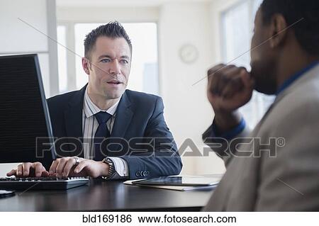 Businessmen talking at desk in office View Large Photo Image Stock Photograph - Businessmen talking at desk in office. Fotosearch