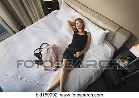 Stock Image - Businesswoman laying on hotel bed. Fotosearch