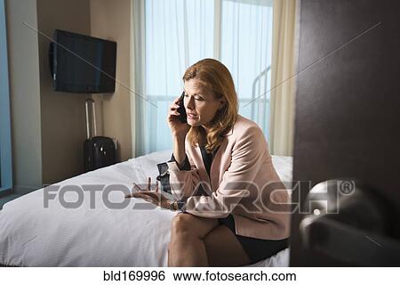 Stock Photograph - Businesswoman talking on cell phone on hotel bed. Fotosearch