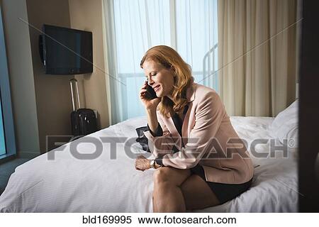 Stock Photography - Businesswoman talking on cell phone on hotel bed. Fotosearch