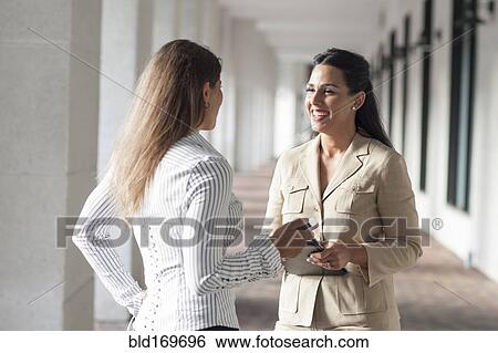 Stock Photograph - Businesswomen talking in hallway. Fotosearch