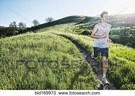 Stock Image - Caucasian athlete running on rural trail. Fotosearch