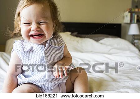 Stock Image - Caucasian baby girl laughing on bed. Fotosearch