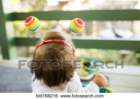 Stock Photograph - Caucasian baby girl on porch wearing multicolor ball headband. Fotosearch