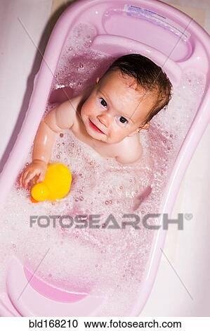 Stock Image - Caucasian baby girl sitting in bathtub. Fotosearch