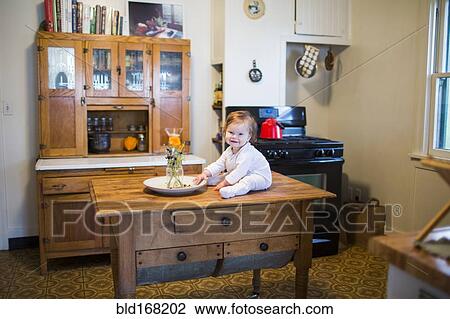Caucasian baby girl sitting on kitchen table View Large Photo Image Stock Image - Caucasian baby girl sitting on kitchen table. Fotosearch