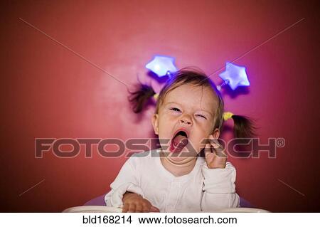 Picture - Caucasian baby girl wearing headband with stars and yawning. Fotosearch
