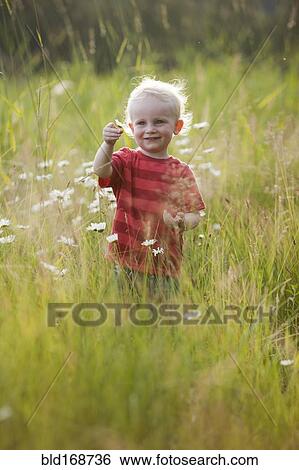 Stock Photograph - Caucasian boy admiring flowers in tall grass. Fotosearch