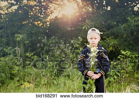 Stock Image - Caucasian boy picking flowers in rural field. Fotosearch