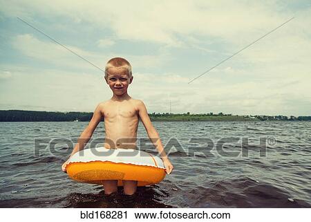 Stock Image - Caucasian boy playing in inner tube in lake. Fotosearch
