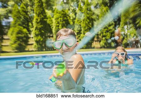 Stock Image - Caucasian boy playing with squirt gun in swimming pool. Fotosearch