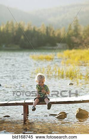 Stock Photography - Caucasian boy sitting on wooden deck over lake. Fotosearch