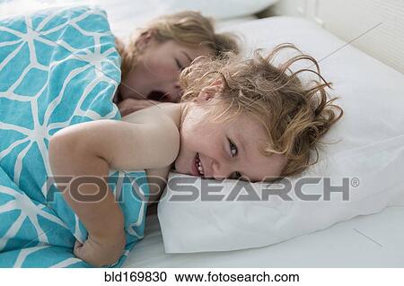 Stock Image - Caucasian brother and sister laying in bed. Fotosearch