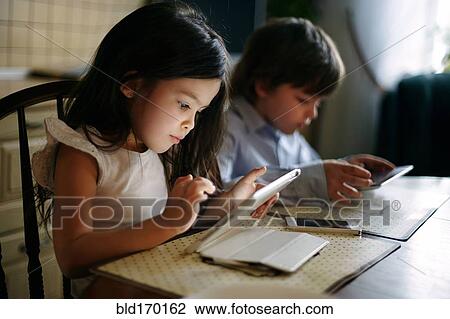 Stock Image - Caucasian brother and sister using digital tablets. Fotosearch
