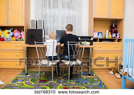 Stock Image - Caucasian brothers using computer in bedroom. Fotosearch