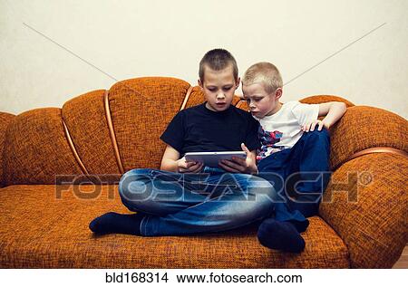 Picture - Caucasian brothers using digital tablet on sofa. Fotosearch