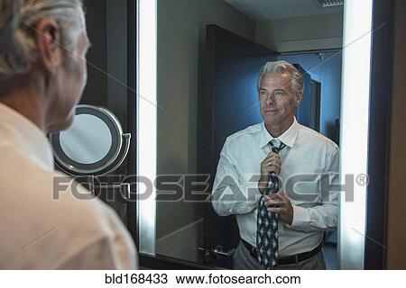 Stock Image - Caucasian businessman adjusting tie in mirror. Fotosearch