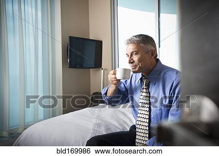 Stock Photograph - Caucasian businessman drinking coffee on hotel bed. Fotosearch