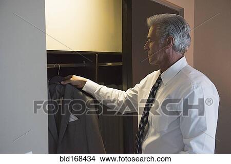 Picture - Caucasian businessman selecting suit from closet. Fotosearch