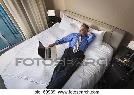 Stock Photo - Caucasian businessman using laptop on hotel bed. Fotosearch