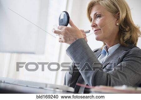 Stock Image - Caucasian businesswoman applying makeup in office. Fotosearch