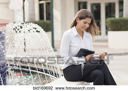 Stock Image - Caucasian businesswoman using cell phone near fountain. Fotosearch