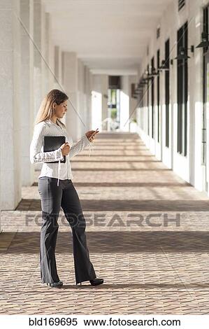 Stock Photography - Caucasian businesswoman using cell phone in hallway. Fotosearch