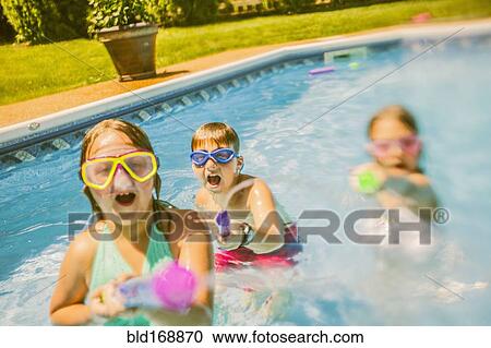 Stock Image - Caucasian children playing with squirt guns in swimming pool. Fotosearch