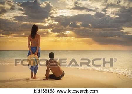 Stock Photo - Caucasian couple admiring sunset on beach. Fotosearch