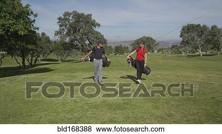 Stock Photo - Caucasian couple carrying golf bags on course. Fotosearch