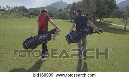 Caucasian couple carrying golf bags on course View Large Photo Image Stock Photo - Caucasian couple carrying golf bags on course. Fotosearch