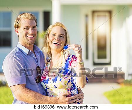 Stock Photograph - Caucasian couple holding keys outside new home. Fotosearch