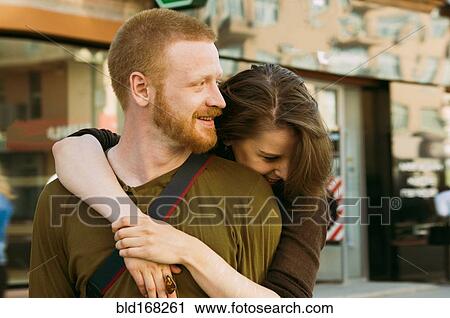Stock Image - Caucasian couple hugging on city sidewalk. Fotosearch