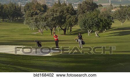 Stock Image - Caucasian couple playing golf on course. Fotosearch