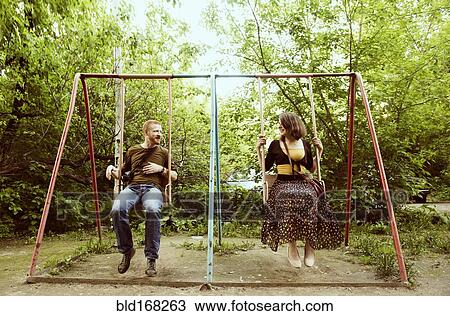 Stock Image - Caucasian couple playing on swing set. Fotosearch