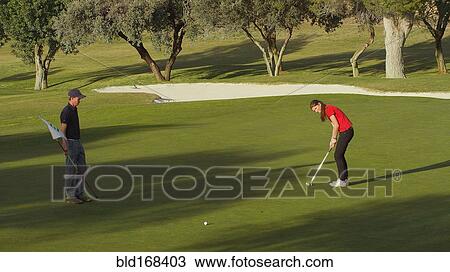 Stock Image - Caucasian couple putting on golf course. Fotosearch