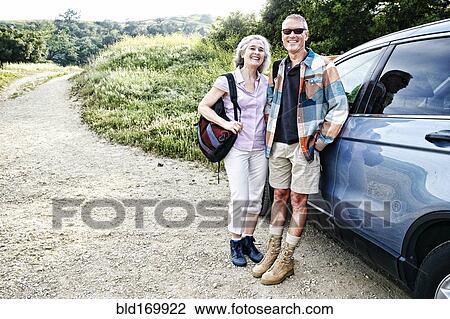 Stock Image - Caucasian couple smiling at car on hiking trail. Fotosearch