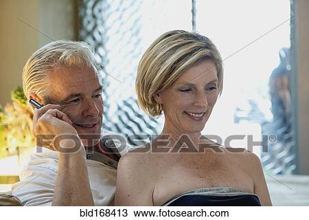 Stock Image - Caucasian couple talking on cell phone in hotel lobby. Fotosearch