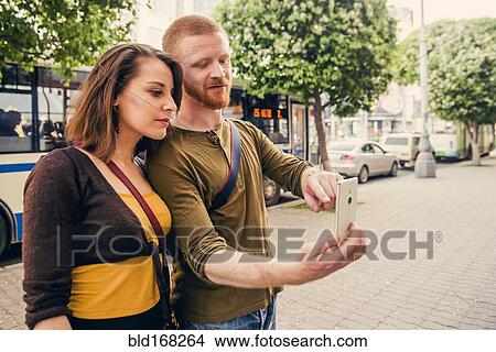 Picture - Caucasian couple using cell phone on city sidewalk. Fotosearch