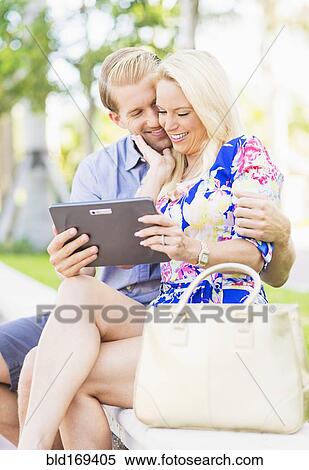 Stock Photography - Caucasian couple using digital tablet on bench. Fotosearch