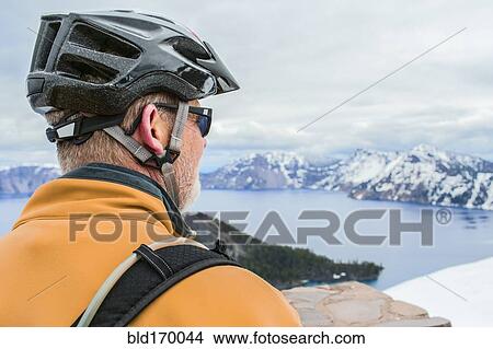 Picture - Caucasian cyclist admiring view of Crater Lake, Oregon, United States. Fotosearch