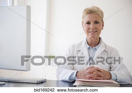 Stock Image - Caucasian doctor sitting at office desk. Fotosearch