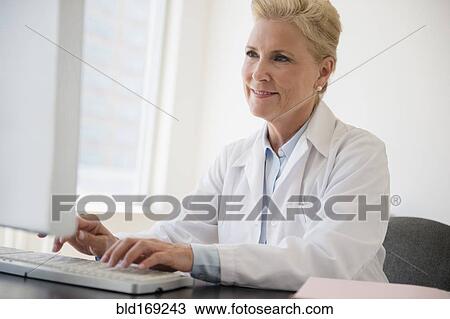 Stock Image - Caucasian doctor working at computer in office. Fotosearch