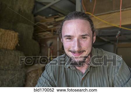 Stock Image - Caucasian farmers smiling in barn. Fotosearch