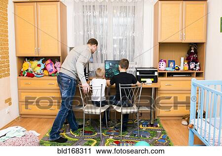 Stock Image - Caucasian father and sons using computer in bedroom. Fotosearch