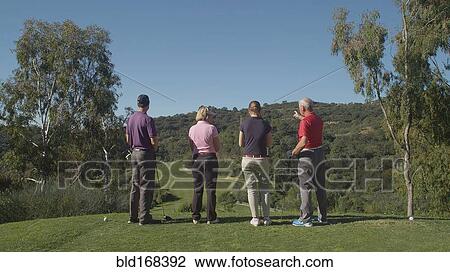 Stock Image - Caucasian friends examining fairway on golf course. Fotosearch