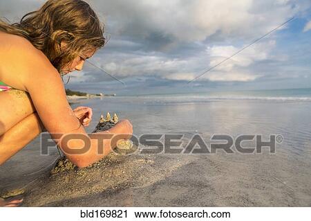 Stock Image - Caucasian girl building sandcastle on beach. Fotosearch