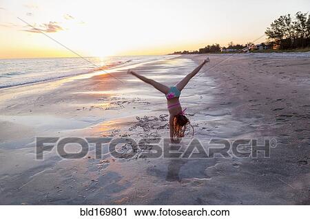 Stock Image - Caucasian girl doing cartwheels on beach. Fotosearch